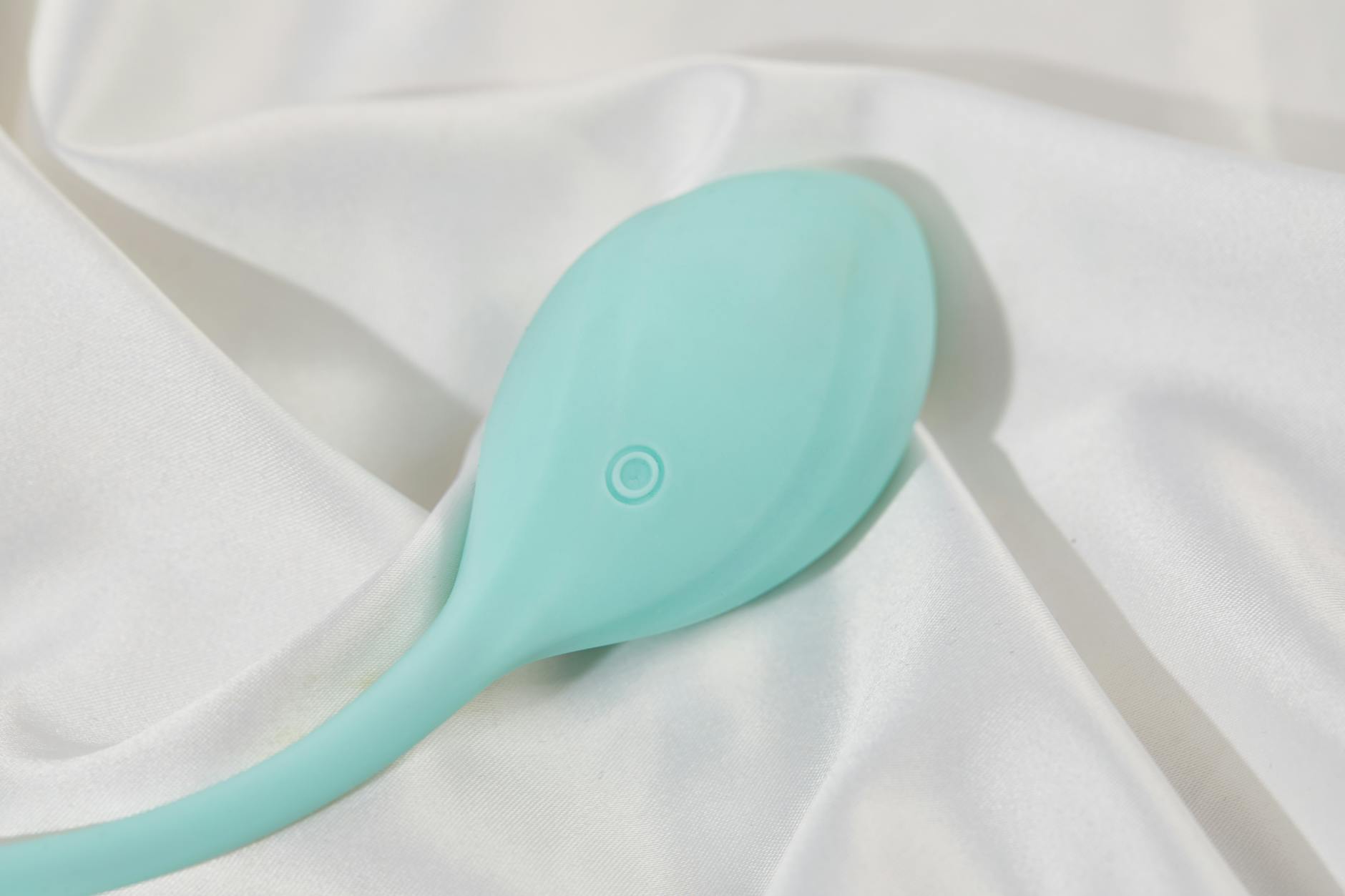A sleek teal lemon vibrator on smooth white silk fabric