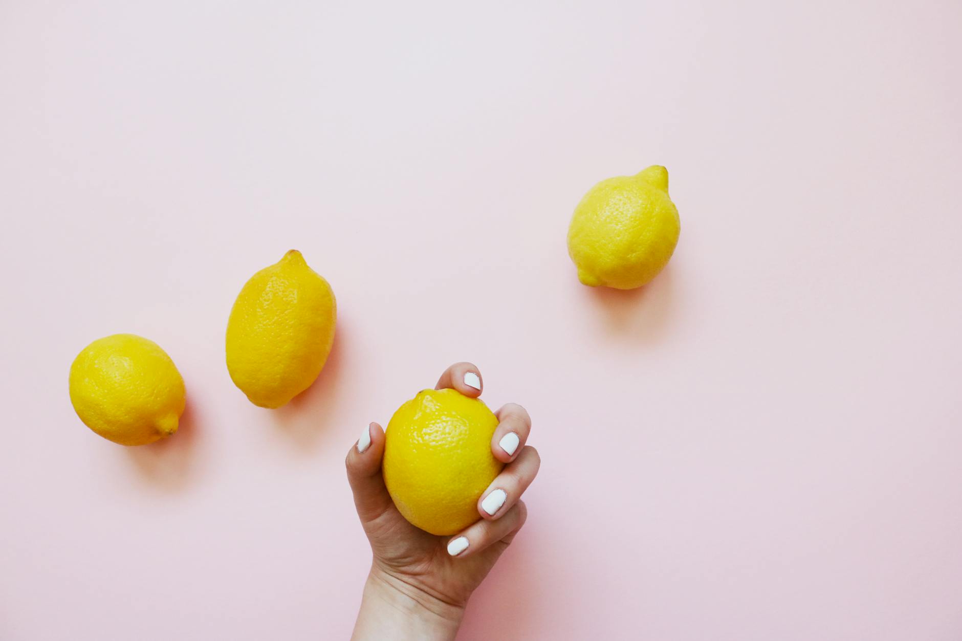 A hand holding a bright yellow lemon on a soft pink background, representing fresh approaches to pleasure and pelvic health