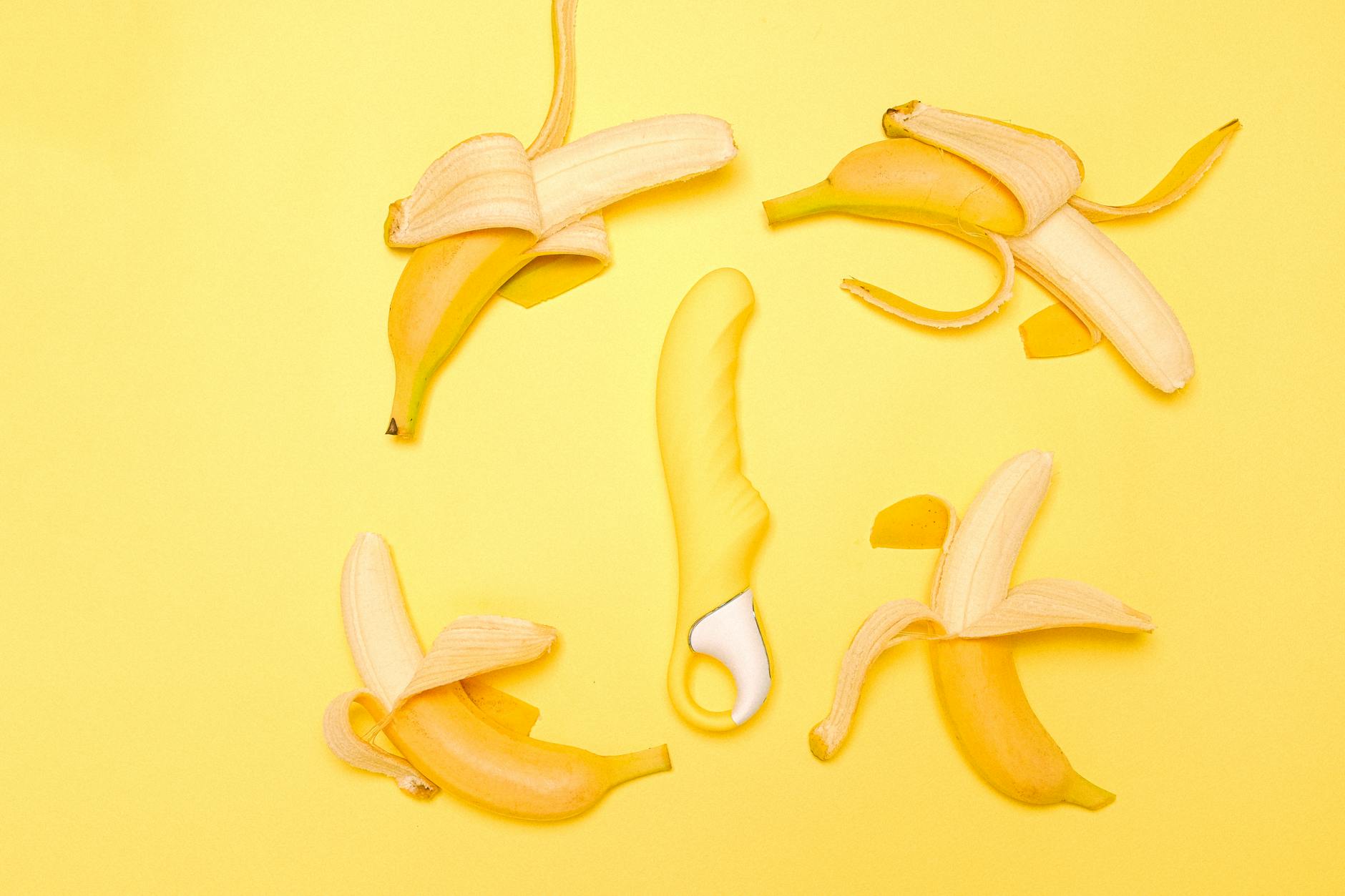 Yellow silicone clitoral vibrator surrounded by fresh lemons on a bright yellow background