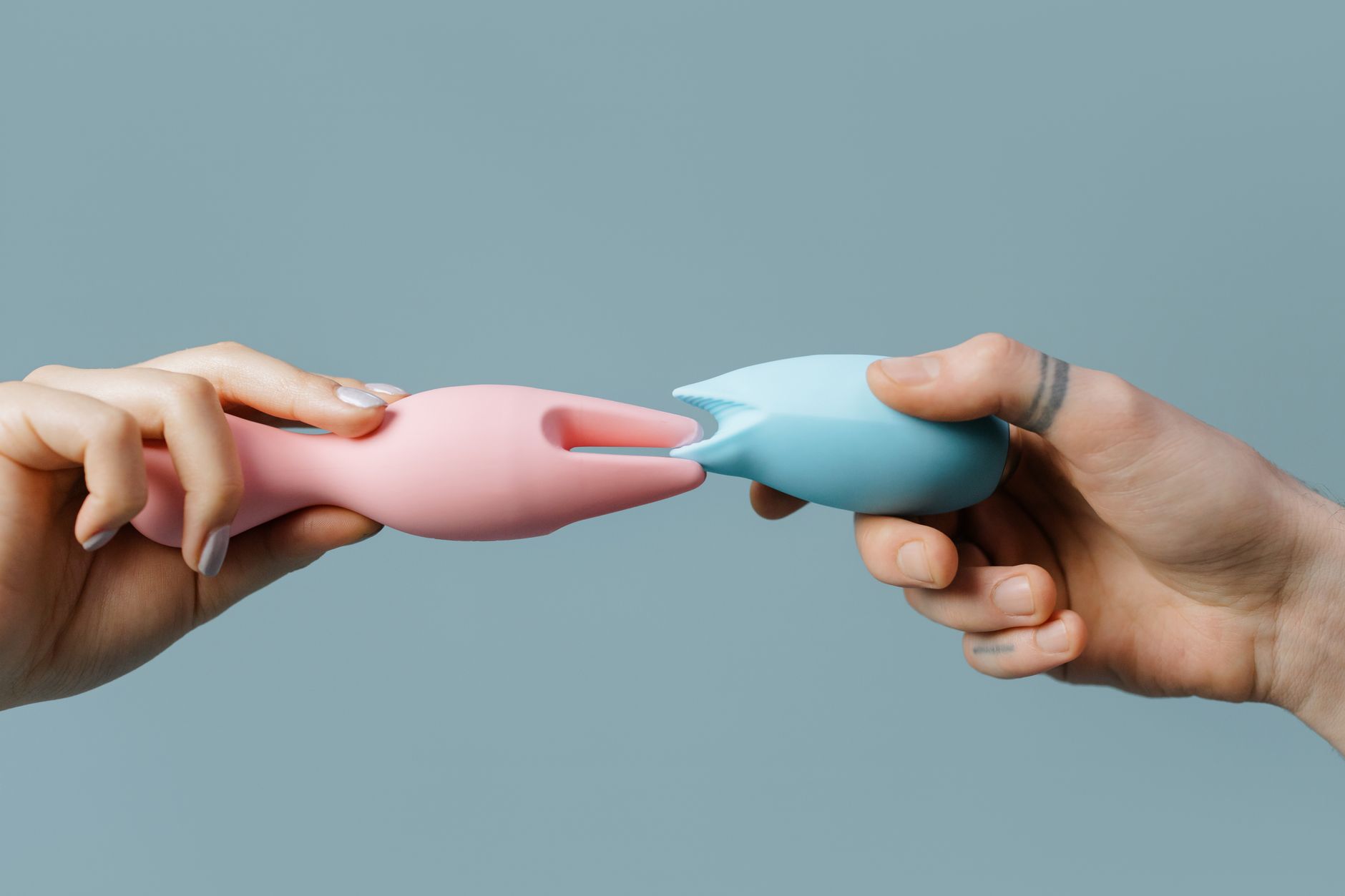 Woman with glasses holding blue and pink silicone vibrators in a thoughtful pose