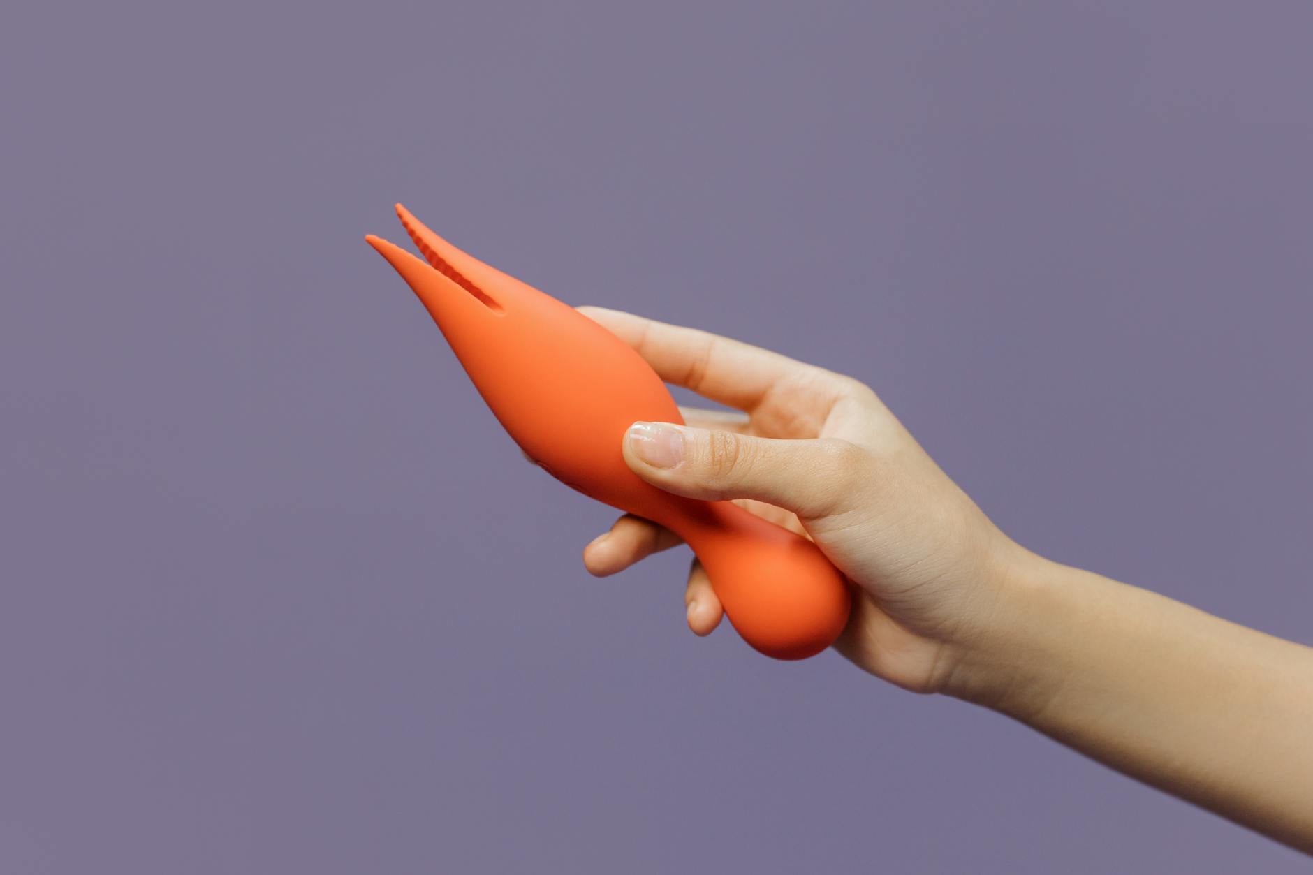 A hand holding a colorful lemon clitoral vibrator against a purple backdrop, showcasing sensual design