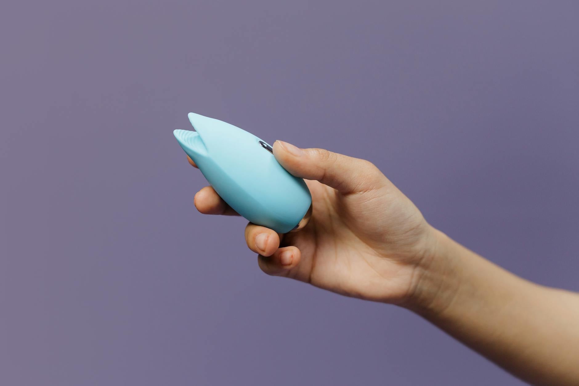 A person holding a blue silicone lemon vibrator against a purple background