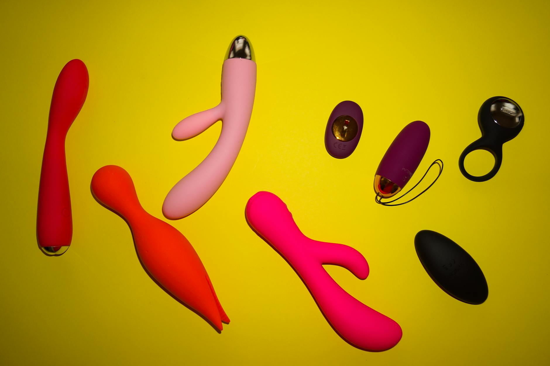 Vibrant array of colorful sex toys including lemon vibrators arranged on a bright yellow surface